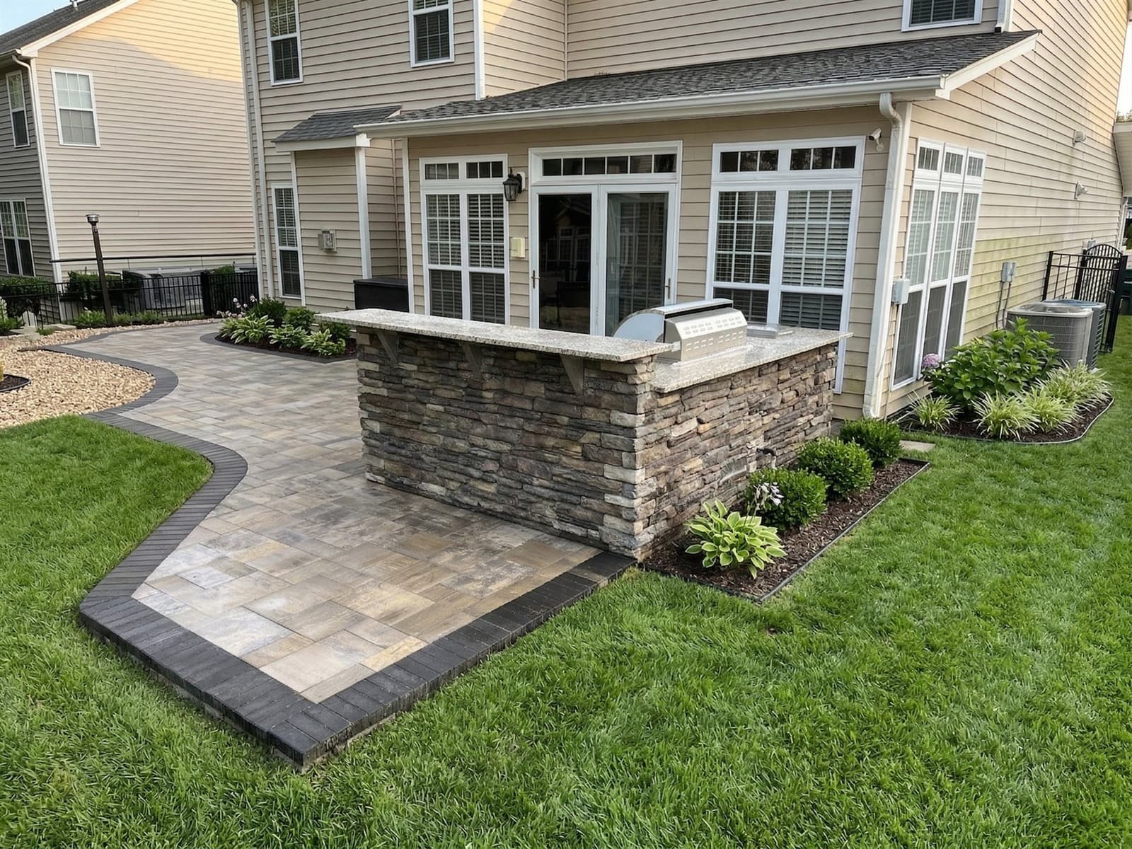 Built-in outdoor kitchen with stone veneer and a granite counter on a Charlotte paver patio
